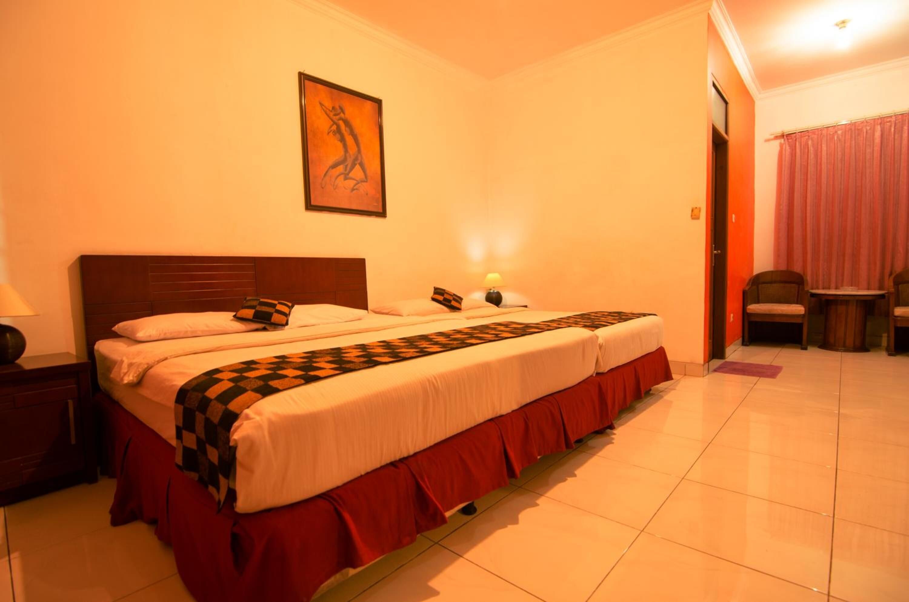 A neatly made bed with a patterned bedspread and pillows, a nightstand with a lamp, and a painting on the wall.