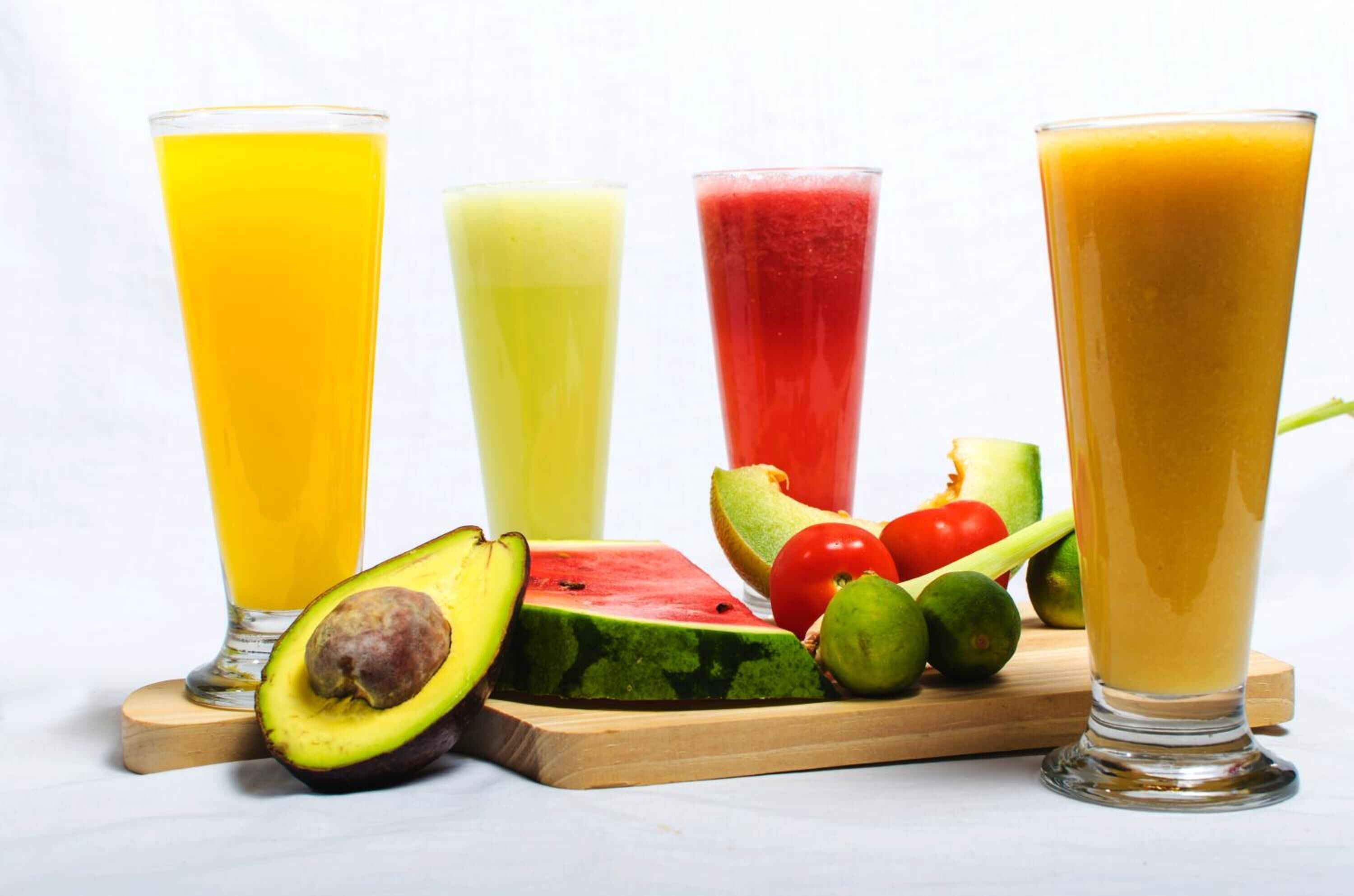 Four glasses of juice and fresh fruits on a wooden board.