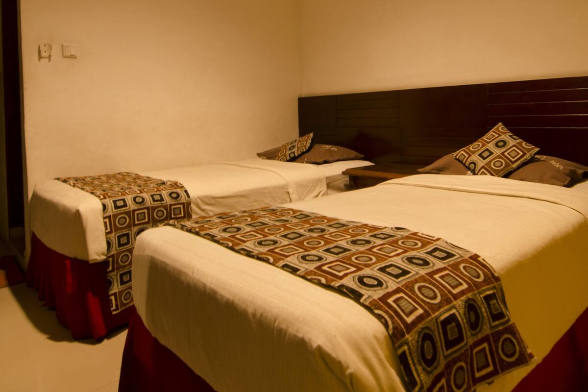 A hotel room with two beds, each with patterned bedding and red curtains.