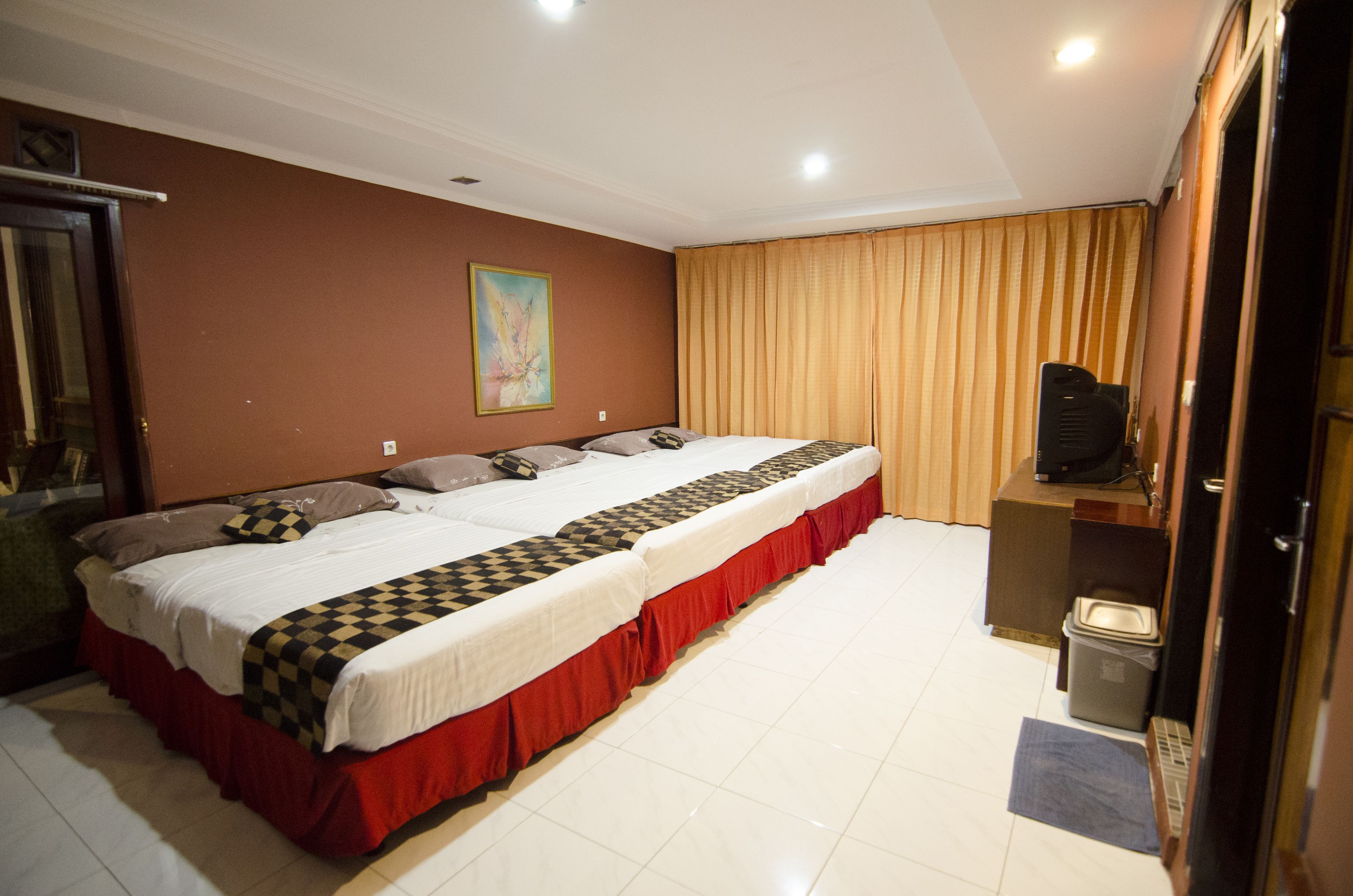 A hotel room with a large bed, a television, and a trash bin.