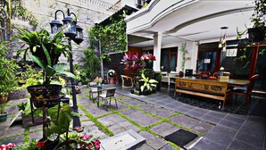 A courtyard with a wooden table and chairs, surrounded by potted plants and a variety of flowers. - Fora Guest House Taman Lingkar (Bandung)