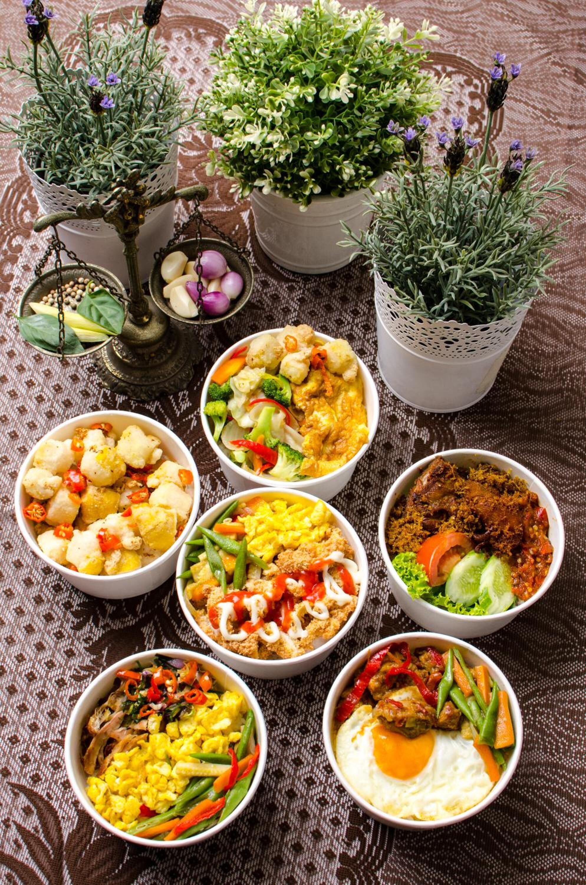 Une table avec sept bols remplis de nourriture et trois plantes en pot.