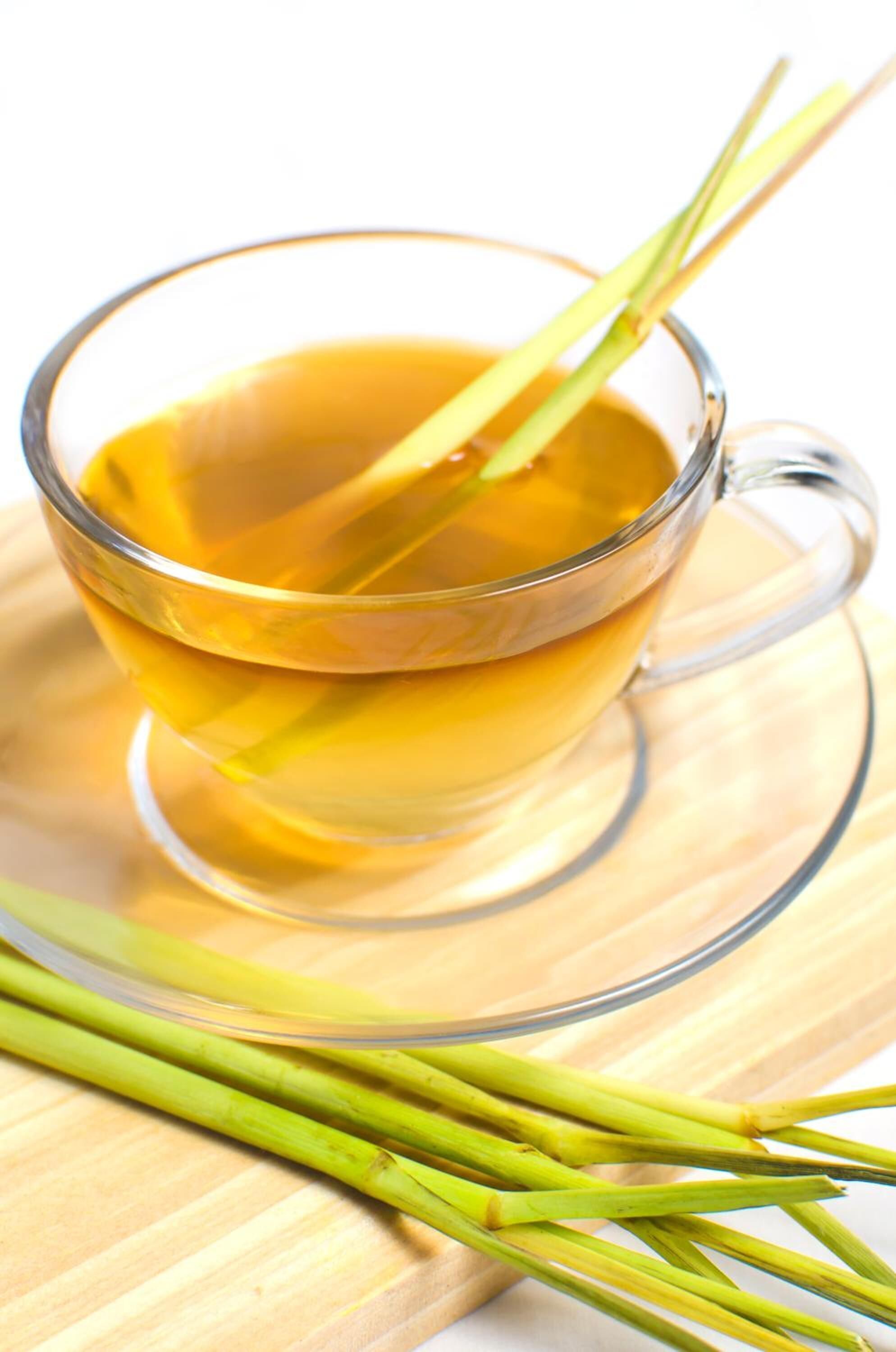 A clear glass cup of yellow liquid with a green straw, placed on a wooden surface.