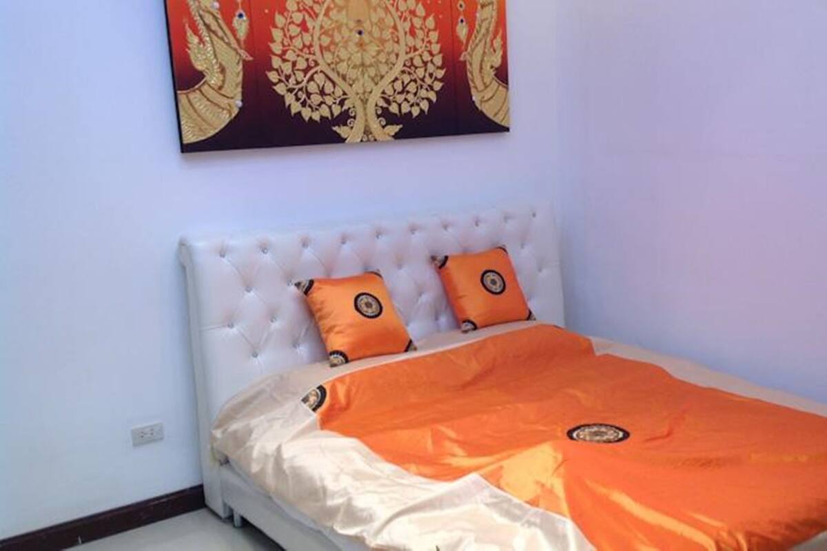 A bedroom with a white tufted headboard, two orange pillows, and an orange bedspread.