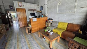 A living room with a wooden coffee table, a brown sofa, a wooden reception desk, and a white brick wall. - Malai Place Lampang (Lampang)