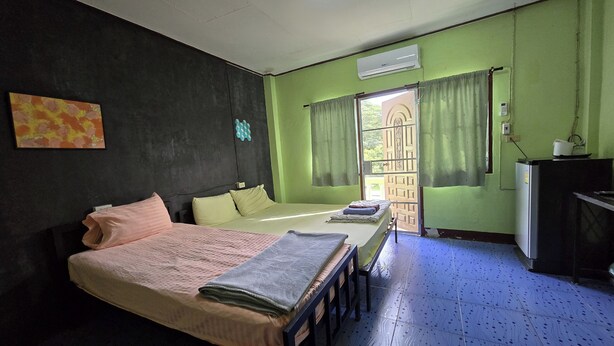 A room with a bed, a desk, a chair, a window with curtains, and an air conditioning unit. - Malai Place Lampang (Lampang)