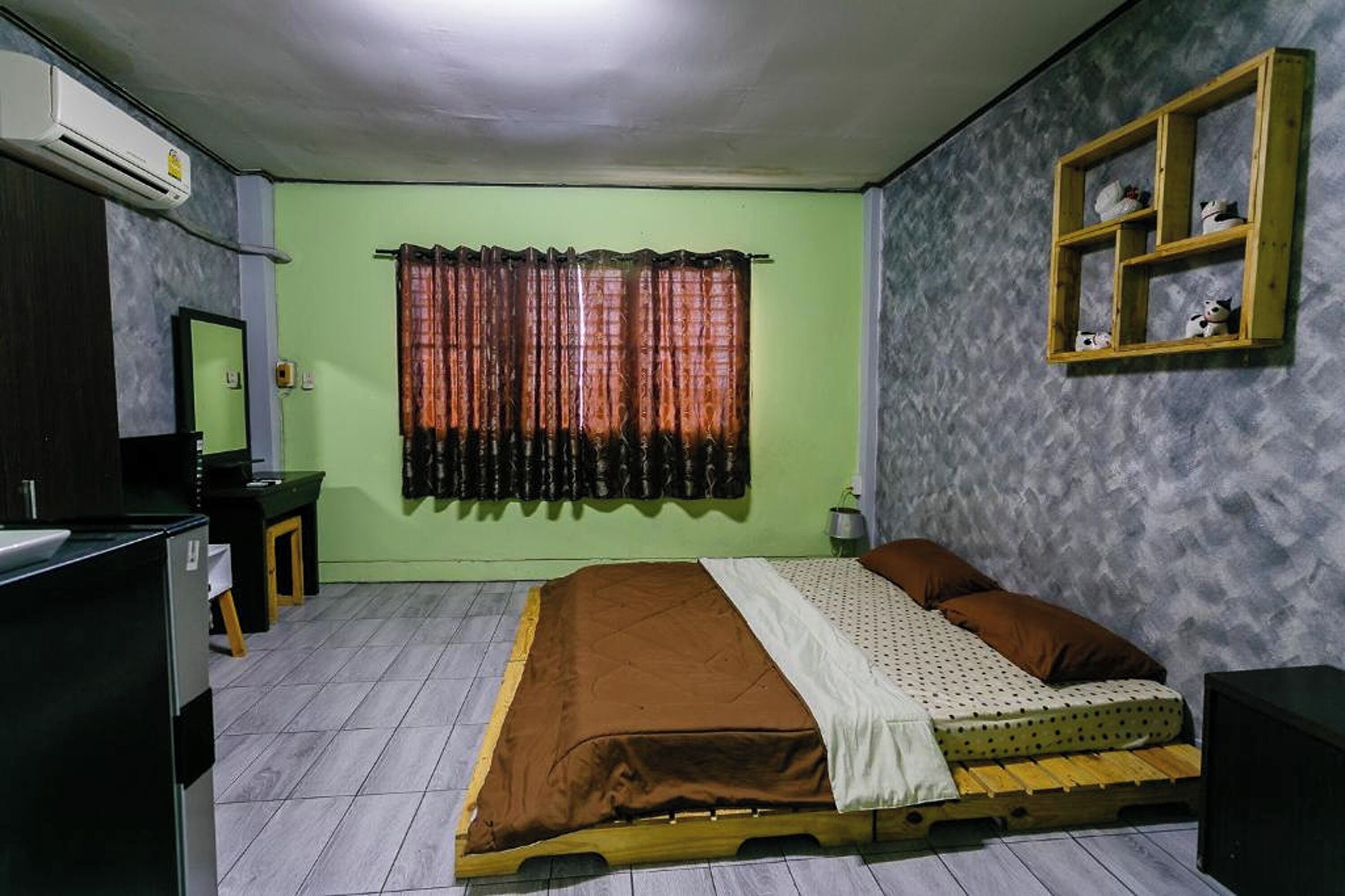 Une chambre à coucher comprenant un lit, une table de chevet, une commode, un climatiseur, une fenêtre avec des rideaux et une étagère avec des objets décoratifs.
