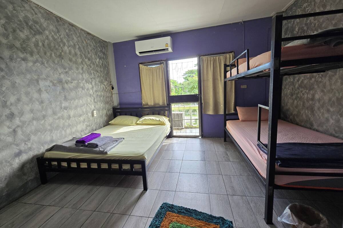 A room with a bunk bed, a single bed, an air conditioning unit, and a window with curtains.