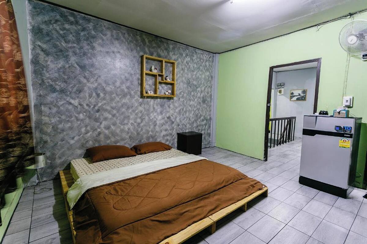 A bedroom with a bed, a small table, a fan, and a wardrobe.