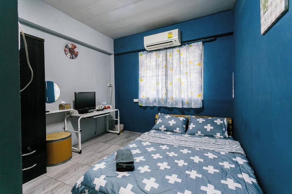 A bedroom with a bed, a desk, a computer, and an air conditioner.