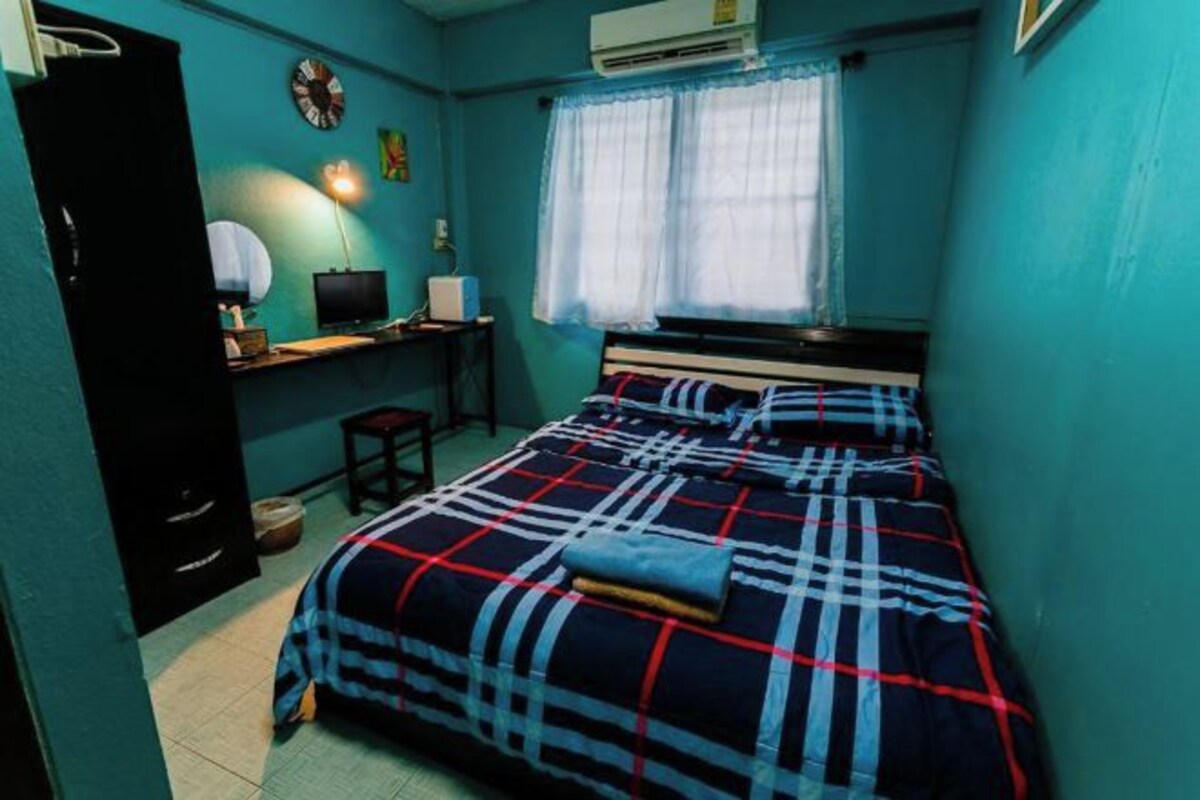 A bedroom with a bed, a desk, a chair, a lamp, and a window with curtains.