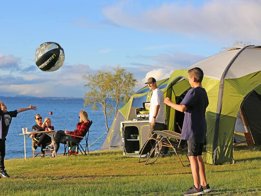 A group of people playing with a ball near a tent and a table by a body of water.