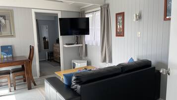 Un saló modern amb un sofà de pell negra, una taula de dinar de fusta amb cadirees, un televisor de pantalla plana muntat a la paret i una taula auxiliar blanca.