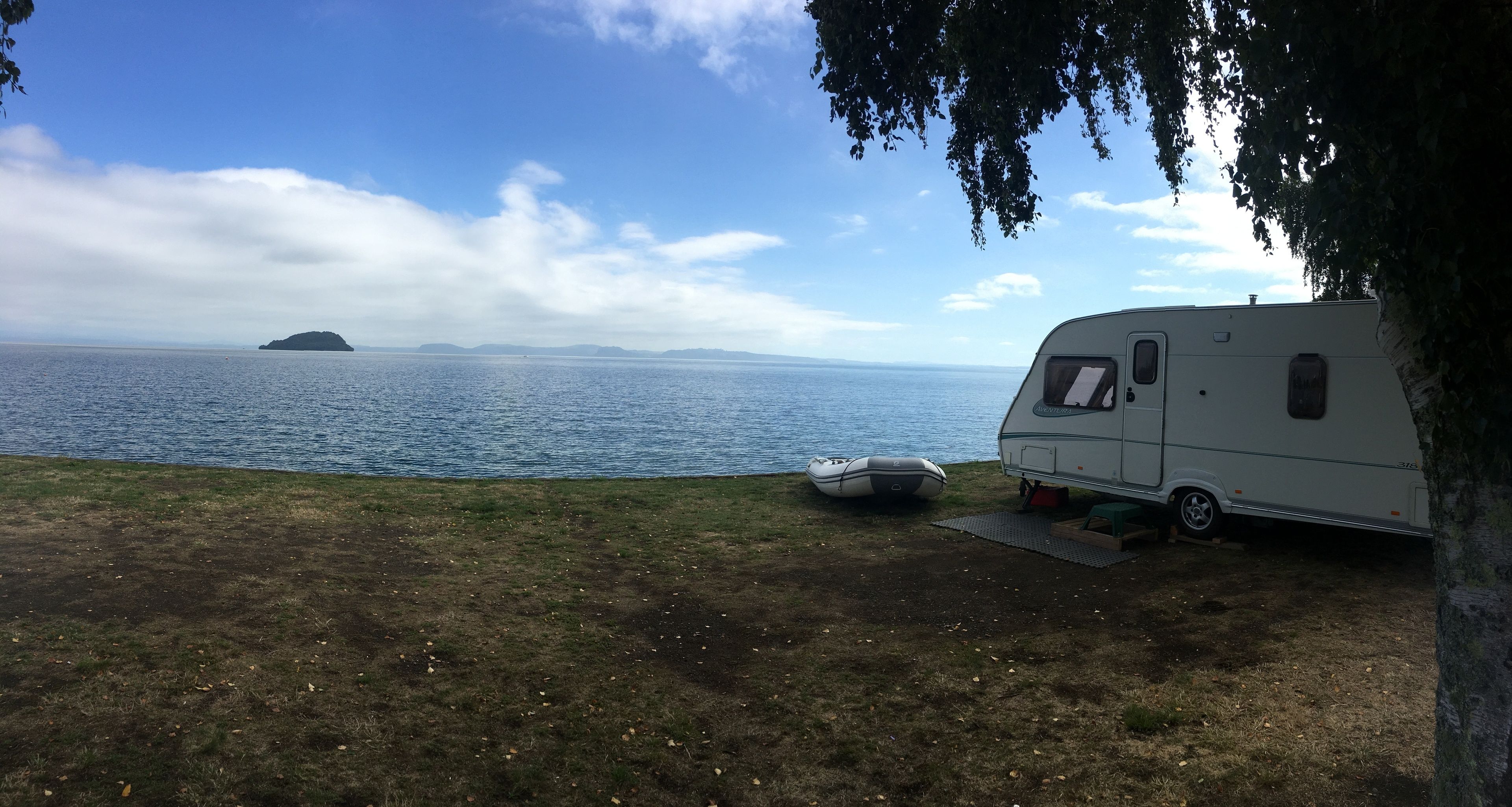 A white RV parked by a lake with a clear sky and distant islands.