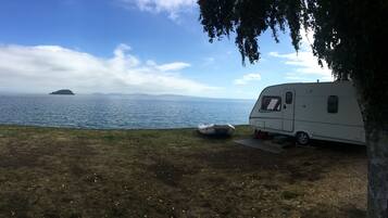 A white RV parked by a lake with a clear sky and distant islands.