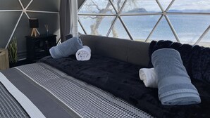 A cozy room with a large window, a bed, a small table with a lamp, and a potted plant. - Motutere Bay Top 10 Holiday Park (Motutere)