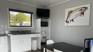 A modern kitchen with white cabinetry, a black countertop, and a dining area with white chairs. - Motutere Bay Top 10 Holiday Park (Motutere)