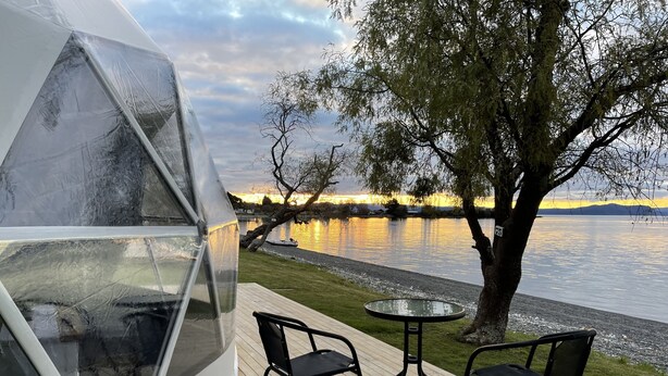 A geodesic dome structure with a view of a lake and sunset. - Motutere Bay Top 10 Holiday Park (Motutere)