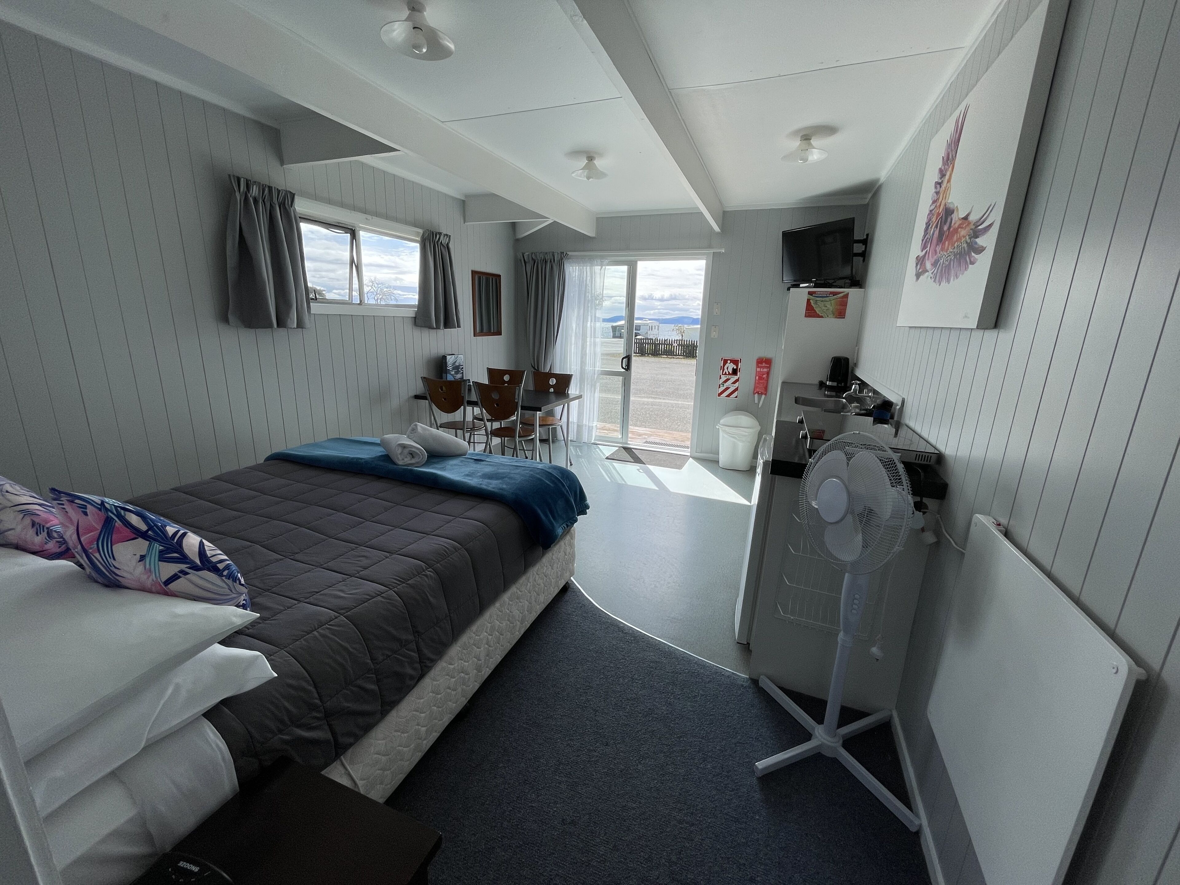 A hotel room with a bed, a desk, a chair, a TV, and a view of the outside.