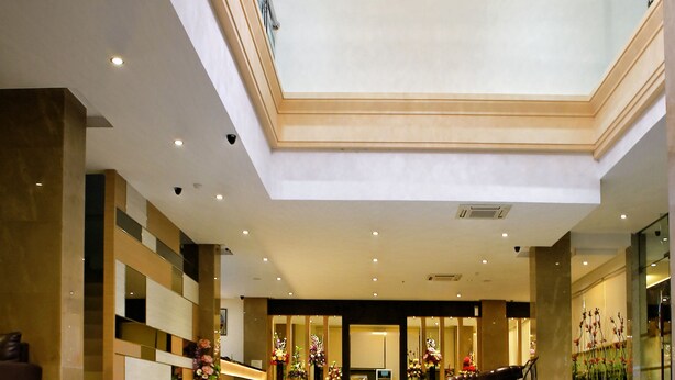 A spacious lobby with a high ceiling, a reception desk, seating area, and a large chandelier.
