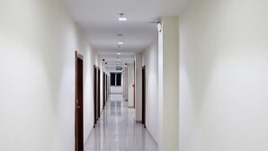 A long, narrow hallway with white walls and a tiled floor, leading to multiple doors.