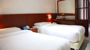 Habitación de hotel con dos camas individuales, cabecera de madera, mesita de noche con lámpara, espejo y estante pequeño con artículos de aseo.