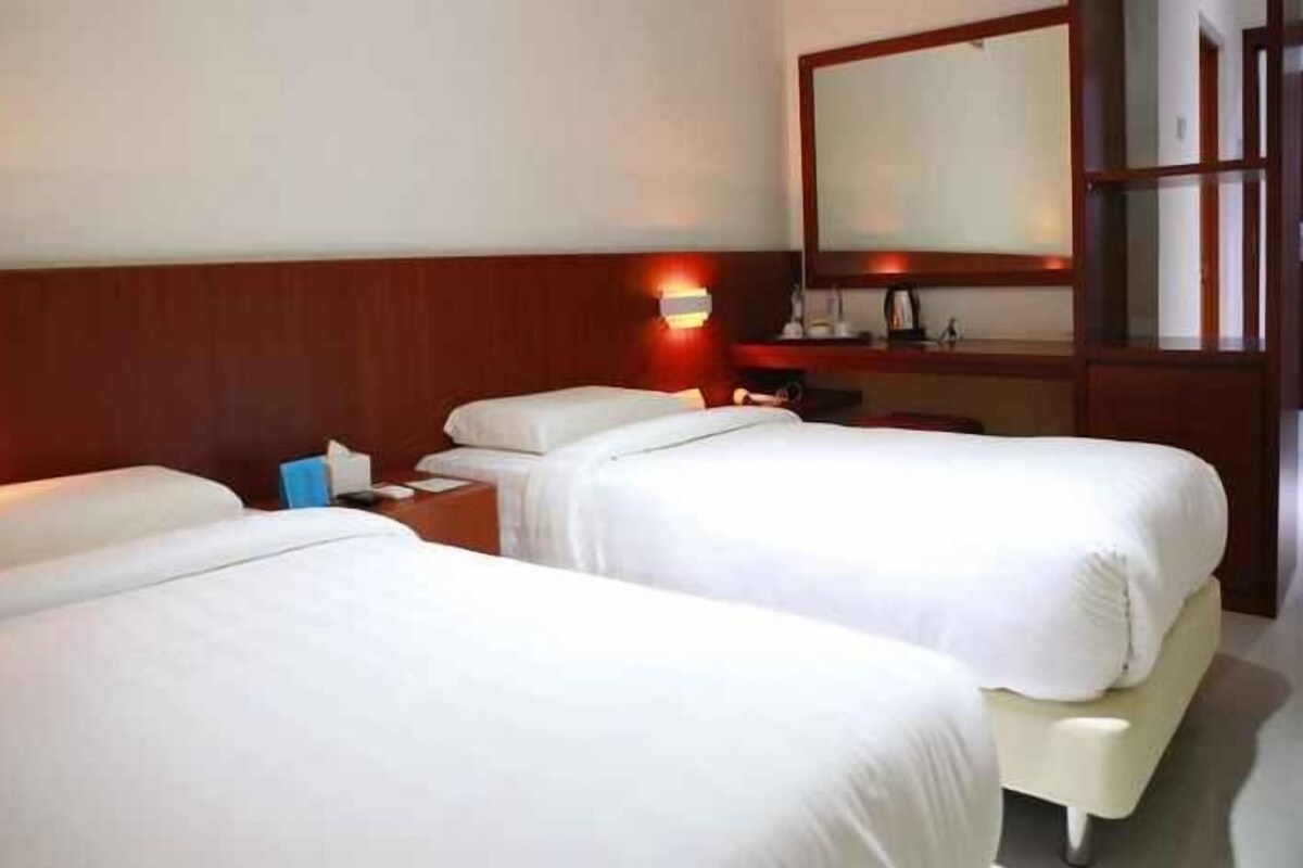 Habitación de hotel con dos camas, una mesita de noche, un espejo y una lámpara fijada a la pared.