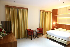 A hotel room with a bed, two chairs, a small table, a TV, and curtains. - Aviari Hotel (Batam)