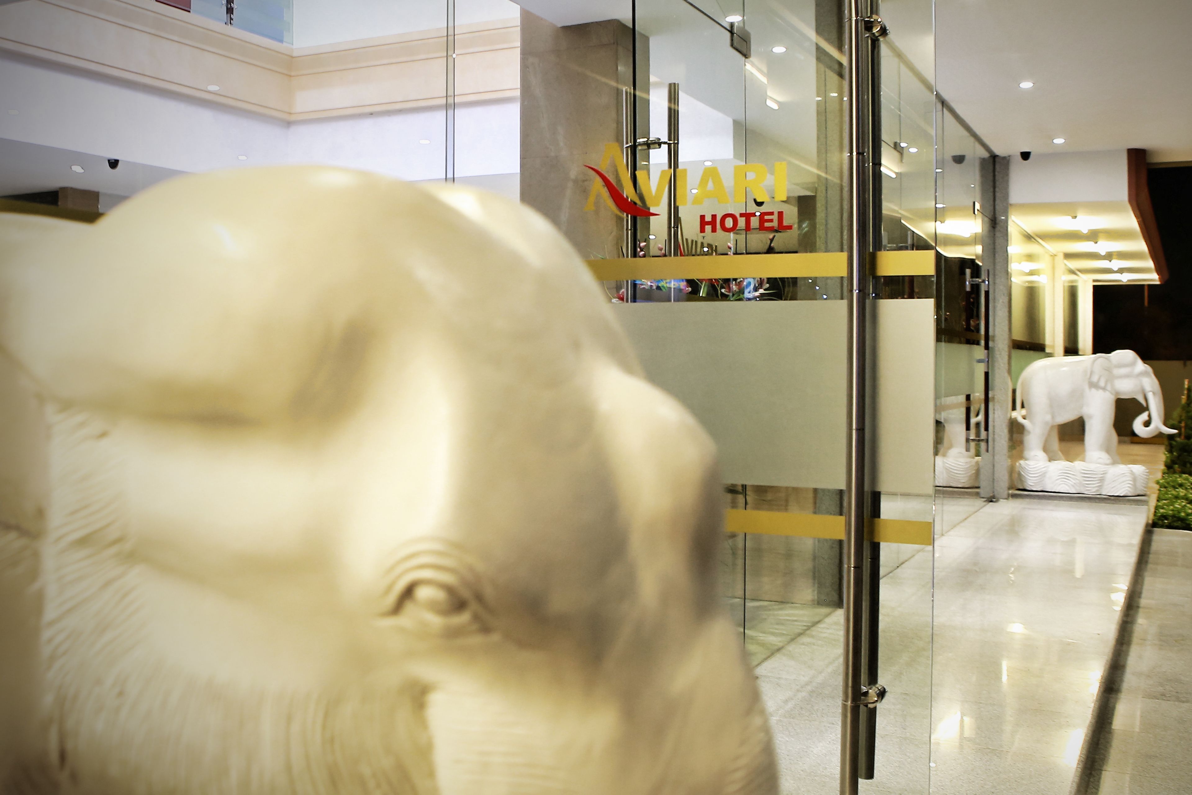 A modern hotel interior with a glass facade, a prominent hotel sign, and a large elephant statue.