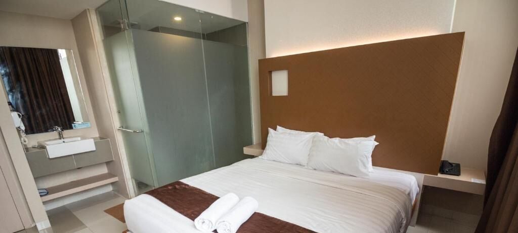 A hotel room with a bed, a glass shower enclosure, a sink, and a mirror.