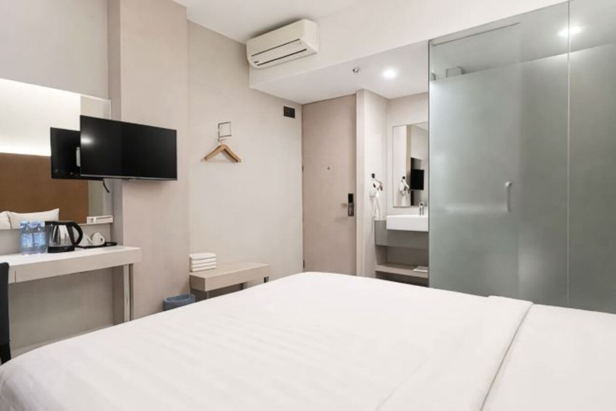 Hotelkamer met een bed, een televisie, een bureau met koffiezetapparaat, een spiegel en een kledingkast.