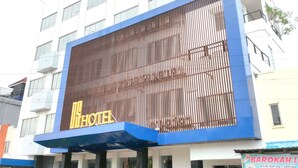 Un hôtel reconnaissable à son grand panneau « HÔTEL », doté d’une façade moderne avec des lambris en bois verticaux et d’une palette de couleurs bleue et blanche.
