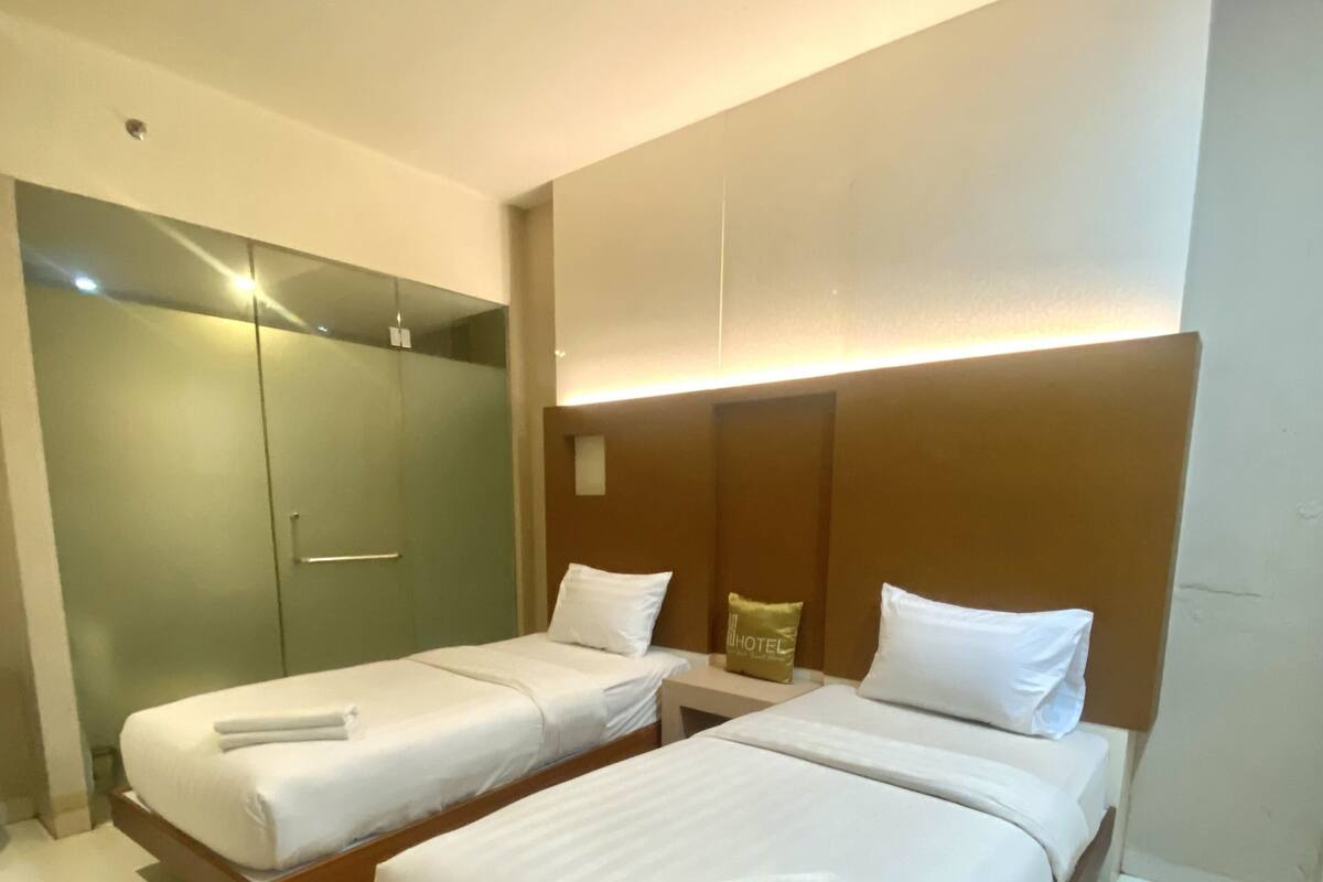 A hotel room with two beds, a wooden headboard, a nightstand, and a mirror.
