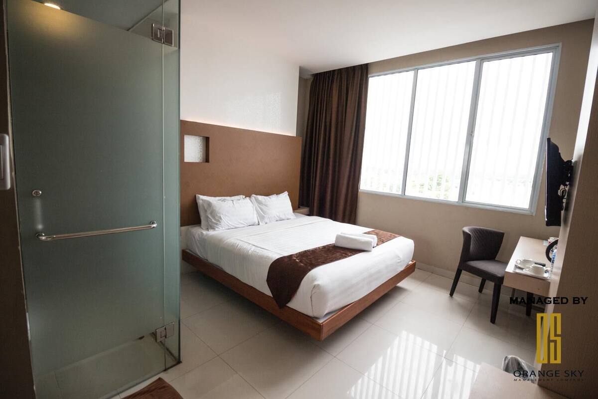 A hotel room with a bed, a desk, a chair, and a large window.