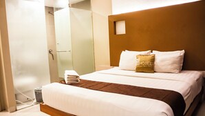 Une chambre d’hôtel avec un grand lit, une tête de lit en bois et une cabine de douche en verre.