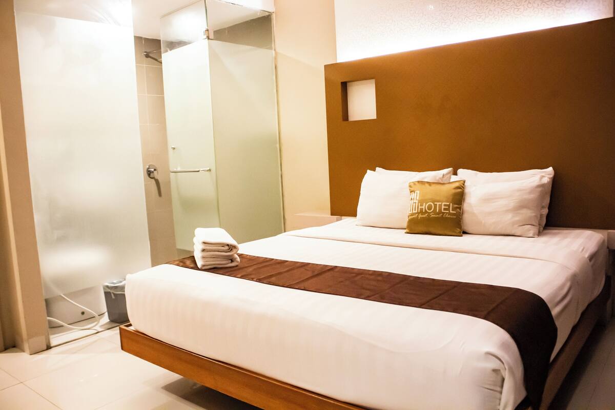 A hotel room with a large bed, a wooden headboard, and a glass shower enclosure.