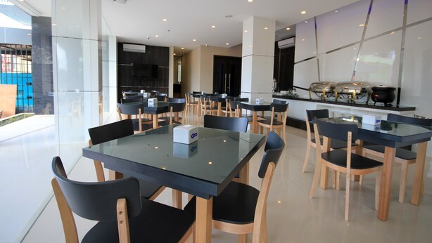 Un espace repas moderne avec des tables en verre et des chaises noires, comprenant un coin cuisine avec des appareils en acier inoxydable en arrière-plan.