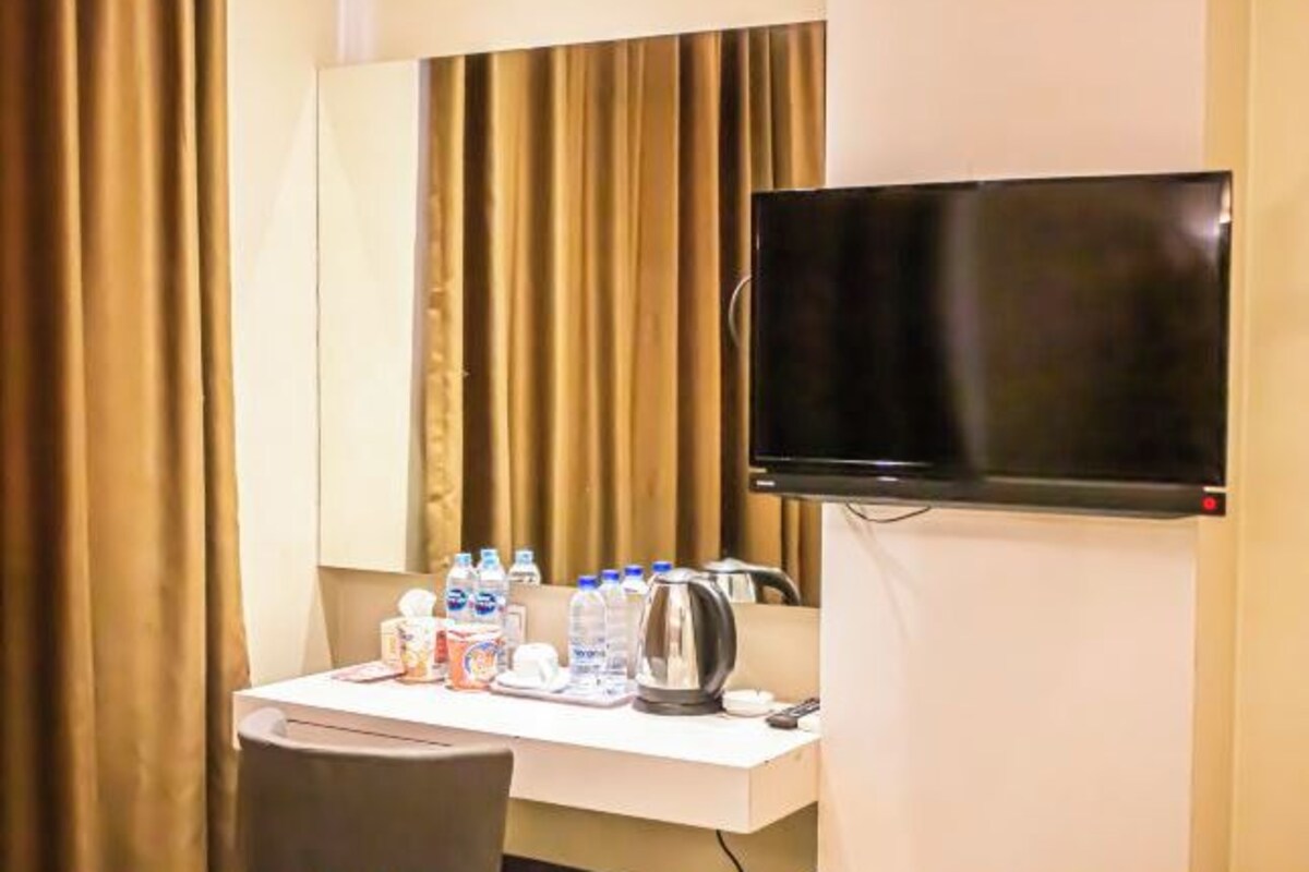 Een hotelkamer met een flatscreen televisie aan de muur, een bureau met een waterkoker, bekers en flessenwater.