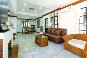 A living room with a brown leather sofa, a wicker coffee table, and a dining area with wooden furniture. - Villa de Nimman (Chiang Mai)
