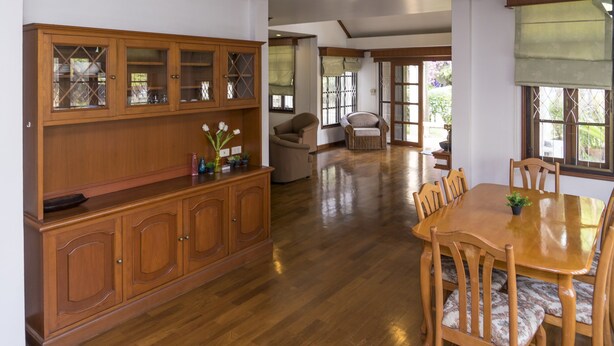 A spacious dining area with a wooden table and chairs, a wooden cabinet with glass doors, and a view of a garden through large windows. - Villa de Nimman (Chiang Mai)