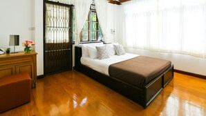 A bedroom with a bed, a wooden bench, a nightstand, a vase with flowers, and a window with curtains. - Villa de Nimman (Chiang Mai)