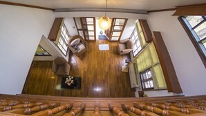 A spacious room with a wooden floor, a high ceiling, and large windows. There are two chairs and a small table with a vase of flowers. - Villa de Nimman (Chiang Mai)