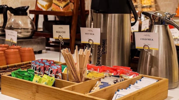 A buffet setup with labeled containers for hot and cold milk, a coffee maker, and a variety of food items in a wooden tray. - Fabhotel Check'in By Oran (New Delhi)