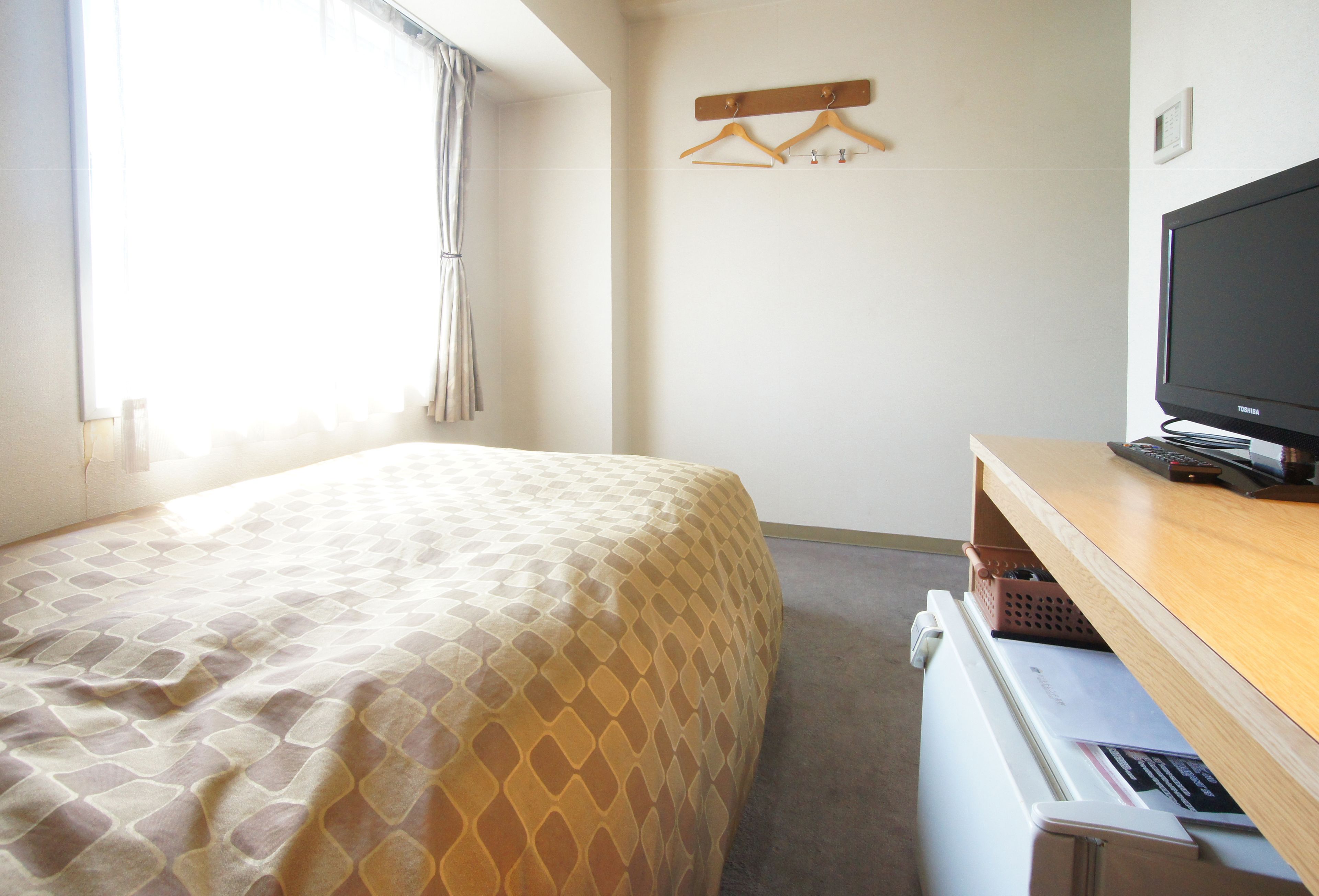 A hotel room with a bed, a TV, a desk with a computer, and a window with curtains.