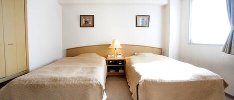 A hotel room with two beds, a nightstand with a lamp, and a window with curtains.