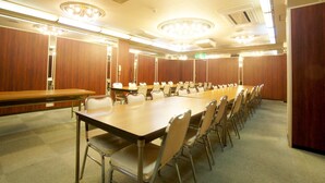 A conference room with a long table and chairs, wooden panel walls, and ceiling lights. - Royal Inn Mito (Mito)
