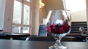 Spiseområde med et glasbord i midten, højt til loftet med altangang i buet glas, og udsigt til naturen gennem store vinduer.