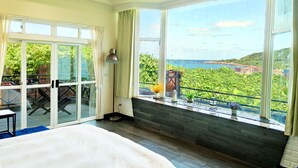 Et soveværelse med en stor seng, en balkon med havudsigt og en skydedør, der fører til et udendørs område.