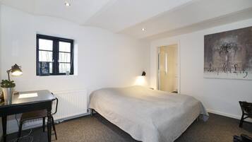Une chambre à coucher avec un lit, un bureau doté d’une lampe, un radiateur, une fenêtre et un tableau accroché au mur.