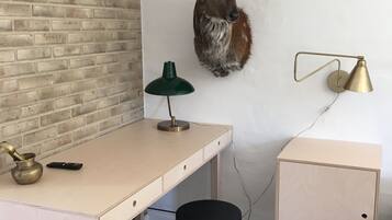 Een kamer met een bakstenen muur, een bureau met een lamp, een kruk en een opgeplakt hert.